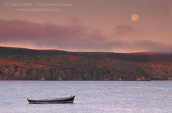 Full moon setting at sunrise over a lone dory in Tomales Bay, Marin County, California