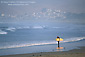 Surfer walking on sandy beach looking at waves, near Morro Bay, Central Coast, California