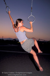 Athletic woman excersises by swinging on rings in evening at Santa Monica Beach, Santa Monica, California