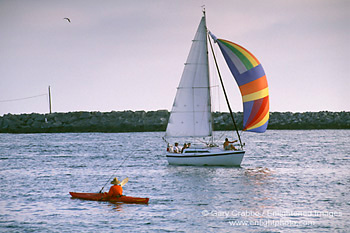 Sailboat passing Lone male adult person fishing from kayak in harbor channel, Newport Beach, Orange County, Southern California Coast