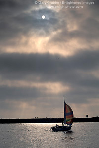 Sailboat sailing in harbor channel and sun and fog at sunset, Newport Beach, Orange County, California