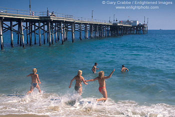 Young girls run into ocean water from sand beach at Balboa Pier, Balboa Island, Newport Beach, California