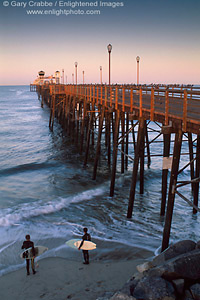 Two young boy surfers checking out the ocean waves at the base of the historic wooden Oceanside Pier, Oceanside, Northern San Diego County Coast, California