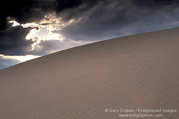 Sunbeams through dark storm clouds over sand dune, near Stovepipe Wells, Death Valley National Park, California; Stock Photo image picture photo Phograph art decor print wall mural gallery