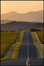 Photo: Golden sunrise light over long straight two lane country road and rolling hills in Spring, Santa Ynez Valley, California