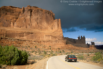 Picture: Car on two lane road belwo red rock cliffs, Arches National Park, Utah