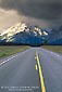 Picture: Straight two lane road below snow covered mountains and storm clouds, Grand Teton National Park, Wyoming