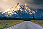 Picture: Straight paved two lane road below snow capped mountains and clearing storm, Grand Teton National Park, Wyoming