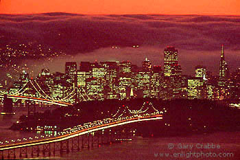 Fog rolling over San Francisco city skyline at sunset behind the Bay Bridge, California